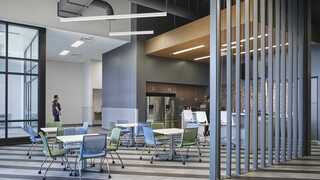 A modern brick building features large glass windows, decorative lighting, and a green rooftop, set against a twilight sky.