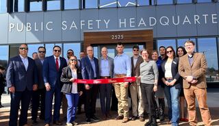 A group of people stands together, smiling and holding a ribbon in front of the newly inaugurated Public Safety Headquarters building.
