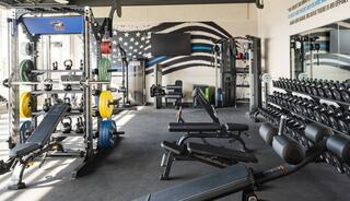 A well-equipped gym featuring various weightlifting machines, benches, free weights, and a motivational wall design.