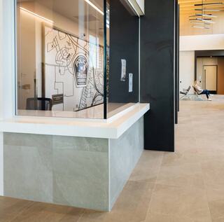 A modern reception area features a service window with a police map behind it, sleek flooring, and a person seated in the background.