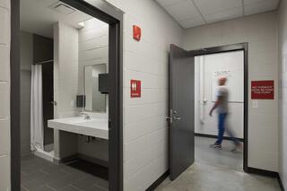 A clean, well-lit restroom area featuring a sink, shower, and a person walking past an open door. Signs indicate restroom usage.