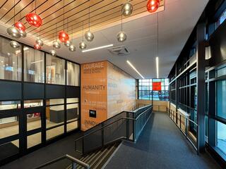 A modern, well-lit hallway features decorative hanging lights and a wall adorned with inspiring words like "Courage" and "Humanity."