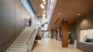 A modern interior space features wide stairs, large windows, and warm lighting, with people engaged in various activities throughout.