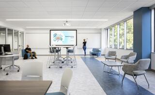 A modern classroom features collaborative seating, a digital screen displaying "Dental Assisting," and natural light from large windows.