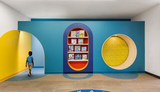A vibrant kids' reading nook features colorful walls with circular cutouts, a bookshelf filled with books, and a child walking through.