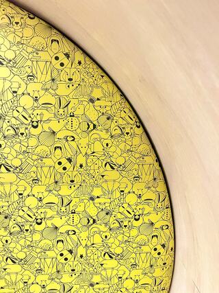 A vibrant yellow surface is filled with intricate black line drawings of whimsical characters and patterns, creating a playful and dynamic scene.