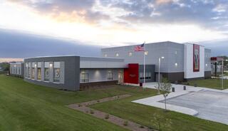 A modern building featuring a sleek design, large windows, an American flag, and ample green space in a serene setting.