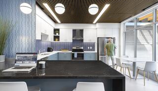 A modern kitchen features sleek cabinetry, a large island, and contemporary lighting, with a person at the fridge and a laptop on the counter.