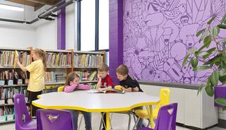 A colorful library scene features children reading at a round table, while another child browses books in a vibrant, engaging environment.