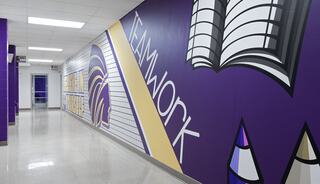 A vibrant hallway features a mural emphasizing "TEAMWORK," alongside colorful illustrations of a book and educational themes.