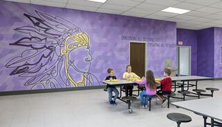 Children sit at tables in a colorful room adorned with a large mural of a Native American chief, emphasizing learning and empowerment.