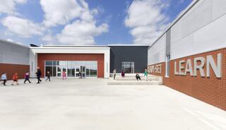 A modern educational building with children walking outside, featuring a welcoming entrance and large "SET LEARN" signage.