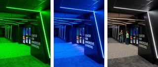 A modern hallway illuminated in varying colors, featuring sleek architecture and signage for an immersive learning center.