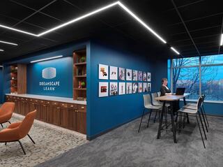 A modern workspace featuring a blue accent wall, framed photos, a sleek wood counter, and comfortable seating, illuminated by stylish lighting.
