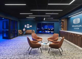 A modern lounge area features stylish chairs, a cozy sofa, and illuminated blue walls, creating a welcoming space for collaboration and learning.