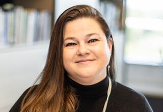 Alyson Sternquist, Vice President and Principal at FGM Architects; A woman with long brown hair and a warm smile, dressed in a black turtleneck, is pictured in a bright, modern setting.