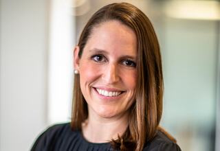 Portrait of Emily Spindler, Vice President and Principal at FGM Architects; woman with straight brown hair, brown eyes, smiling, wearing a black shirt and pearl stud earrings