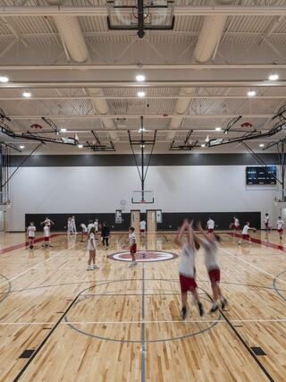 A bright basketball court hosts young players practicing, with some shooting hoops and others engaging in drills, surrounded by a modern gym setting.