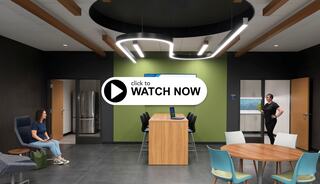 A modern community college lounge space features stylish seating, a central wooden table, and contemporary lighting, creating an inviting atmosphere for collaboration.