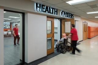 A hallway features "HEALTH CAREERS" signage, with a person in a red shirt pushing a wheelchair into a caring environment.