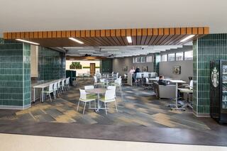 A modern cafeteria with green tile accents, wooden ceiling, varied seating, and a relaxed atmosphere for dining and socializing.