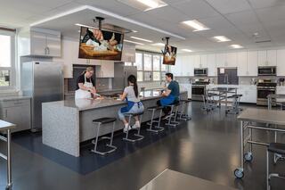 A bright, modern kitchen featuring a chef demonstrating cooking techniques while students observe at a spacious counter with sleek appliances.