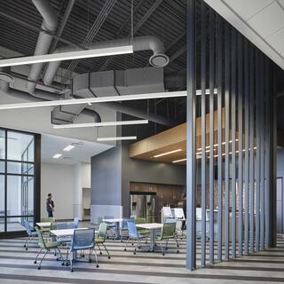A modern two-story building with large windows, illuminated entryway, and a green rooftop, surrounded by a peaceful evening sky.