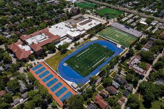 Aerial view of a school campus featuring a football field, tennis courts, and athletic facilities surrounded by residential areas.