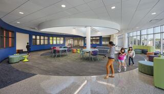 A bright, modern learning space with colorful furniture, circular seating, and children interacting happily in an open, inviting environment.