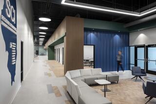 A modern, airy lobby features a stylish gray sofa, blue and green accents, and a person walking towards conference rooms.
