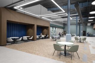A spacious, modern entrance lobby features tables and chairs with wood and blue accents, offering a collaborative atmosphere for socializing and work.