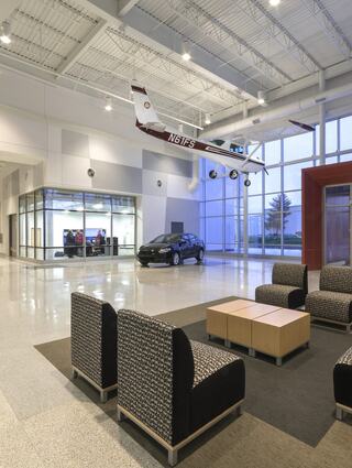 A spacious lobby features modern seating, polished floors, large windows, and a small airplane suspended from the ceiling, adding a unique touch.