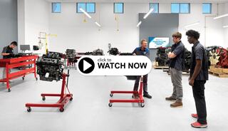 A modern workshop features several engine stands with students and an instructor engaged in hands-on learning about automotive engineering.