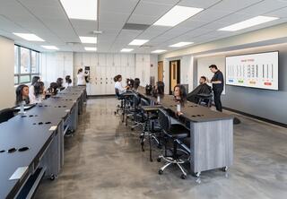 A modern classroom with ergonomic furniture, a large screen displaying data, and students attentively engaging with an instructor.