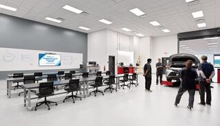 A modern automotive training facility featuring a classroom area and a car with its hood open, with instructors and students engaged in learning.