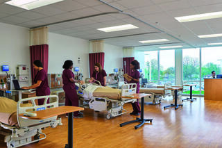A modern healthcare simulation room features healthcare professionals in scrubs attending to patient beds and utilizing medical equipment.