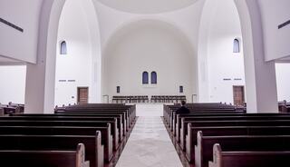 A spacious, modern interior of a church features long wooden pews, arched ceilings, and subtle lighting, creating a serene atmosphere.