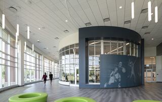 A modern, spacious interior features large windows, sleek lighting, and vibrant seating, highlighting an active environment.