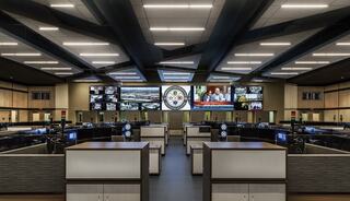 A modern control room features multiple screens displaying information, with sleek workstations arranged in an open layout.