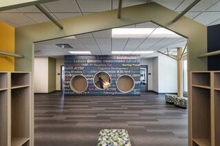 A vibrant, modern educational space with playful design elements, featuring wall graphics, circular openings, and colorful seating.