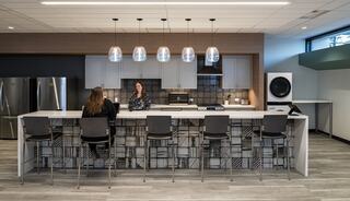 A modern kitchen features sleek appliances, a long island with stools, and pendant lights, creating a welcoming space for conversation.