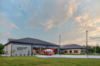A modern fire station featuring a stone facade, multiple garage doors, and clear skies, surrounded by green grass and landscaping.