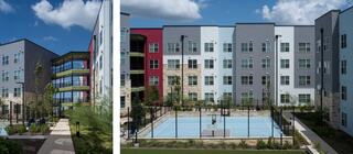 Modern apartment buildings with colorful facades and a fenced basketball court surrounded by greenery under a bright blue sky.