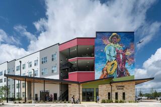 A colorful mural of a cowboy adorns the exterior of a modern learning center, blending contemporary architecture with artistic flair.