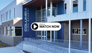 A modern school building features large windows and a welcoming entrance, with a sign indicating "Columbia High School" prominently displayed.