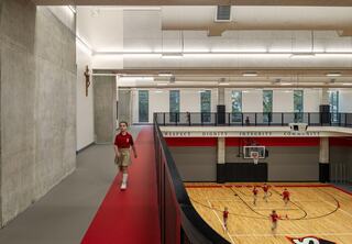A young girl walks along a red walkway overlooking a sports court where children play basketball, reflecting values of respect and community.