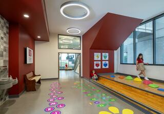 A vibrant educational space features colorful interactive flooring, playful climbing elements, and cheerful children exploring the area.