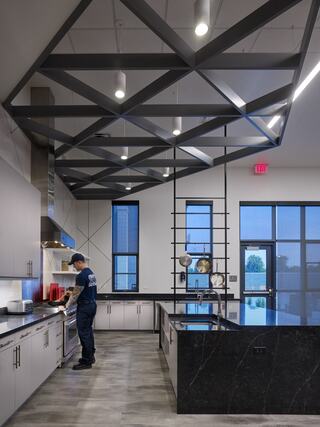 A modern kitchen features sleek cabinetry, a spacious island, and contemporary lighting, with a chef preparing food amidst a stylish design.