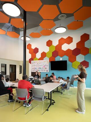 A brightly colored classroom features hexagonal wall decor, a large screen, and a group of children engaged in learning.