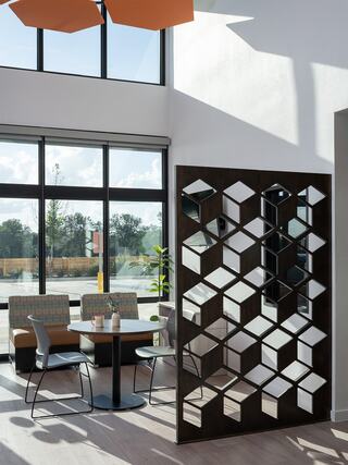 A bright, modern space features large windows, a geometric mirrored partition, and a cozy seating area with a round table.